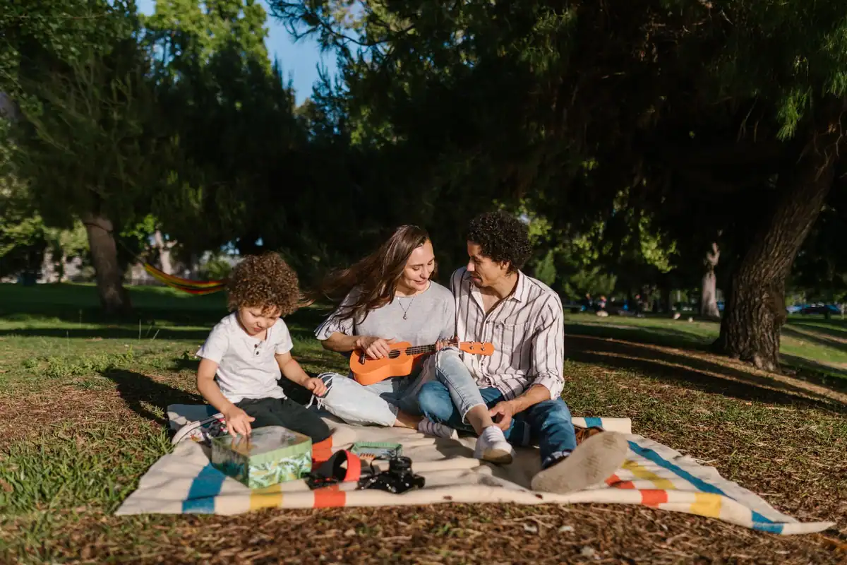 Familie cu un copil mic, așezată pe o pătură la picnic în parc