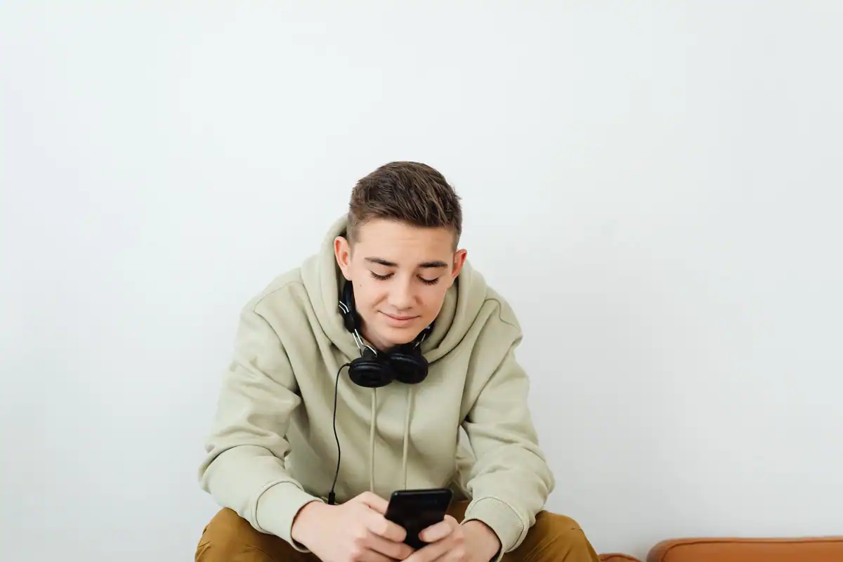 Adolescent cu căști la gât stă pe pat și se uită la telefon