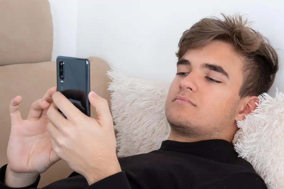 Adolescent întins pe canapea, cu telefonul în mână, în camera lui