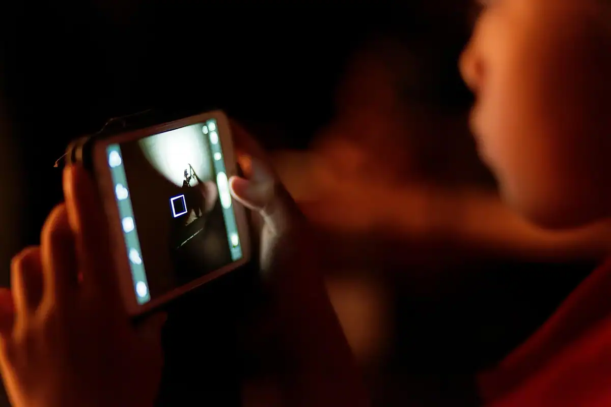 Copil privește ecranul unui telefon mobil, într-o lumină slabă
