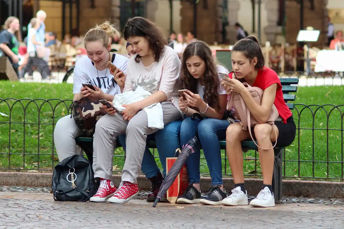 Cinci adolescente stau pe o bancă, fiecare cu privirea în telefon