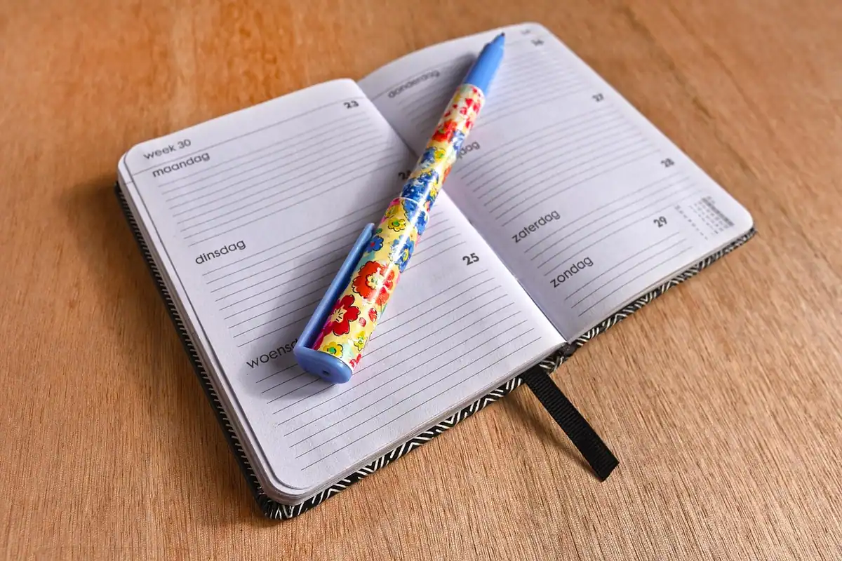 Agendă deschisă, cu un pix colorat, pentru planificarea zilelor