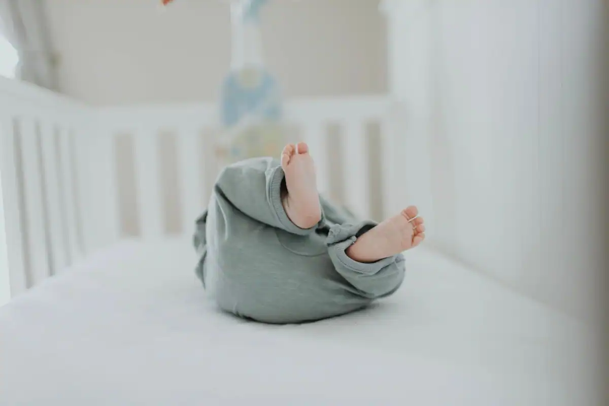 Picioruțele unui bebeluș îmbrăcat în pijama, într-un pătuț alb