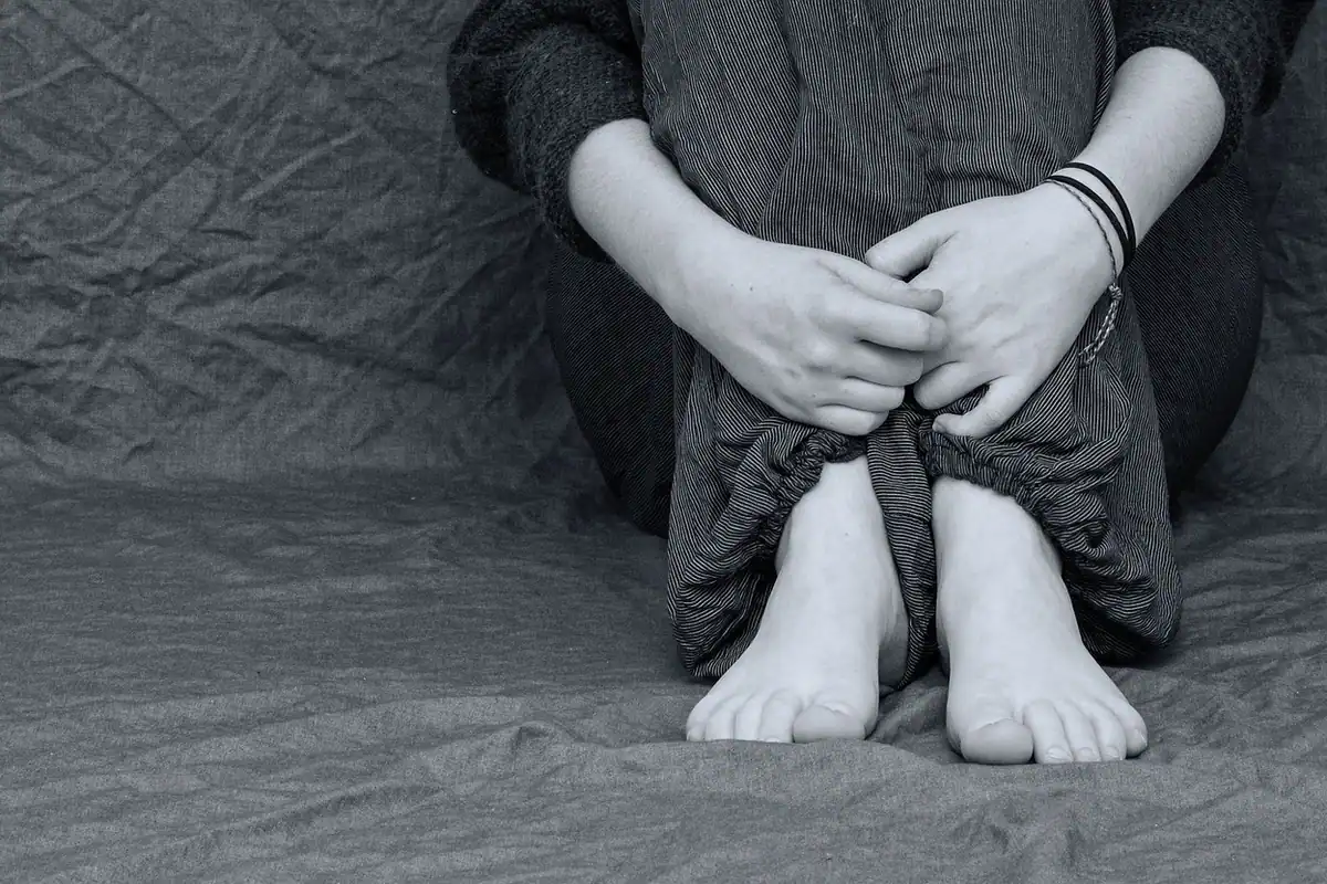 Adolescent ghemuit, cu brațele în jurul genunchilor, într-o stare de neliniște
