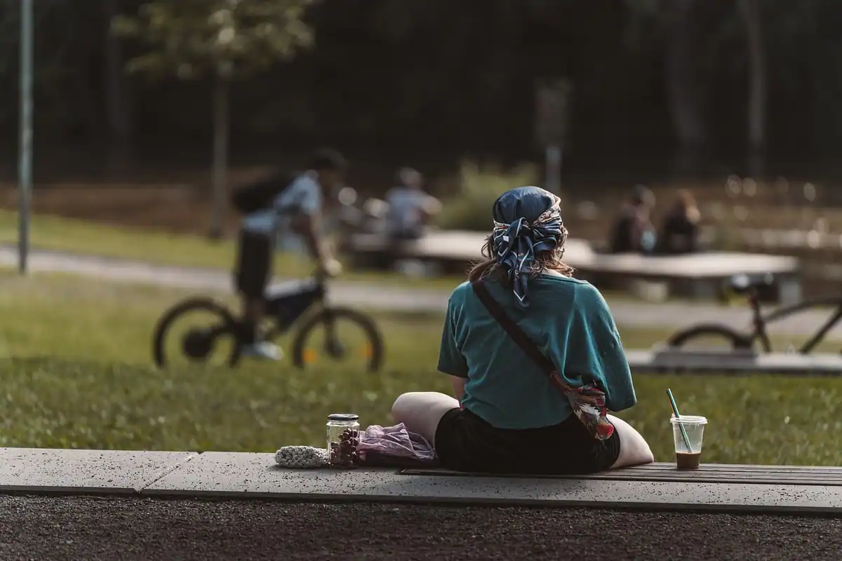 Femeie așezată într-un parc, cu o cafea rece, într-o zi de vară